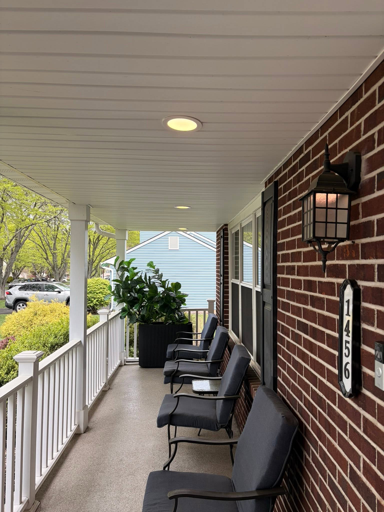 Recessed ceiling lights and a wall lantern along a covered front porch.
